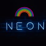 Colorful neon rainbow and text sign against a dark backdrop.